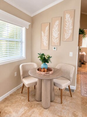 A dining area with a round table, two chairs, a vase with flowers, and three framed leaf artworks on the wall. - The Blue Door: a Be Free Tiny Home (Jacksonville)