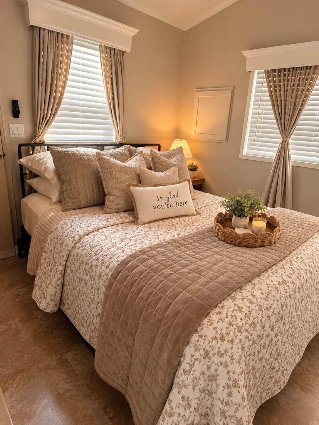 A neatly made bed with a floral-patterned duvet, a decorative pillow with text, and a bedside table with a lamp and a small plant.