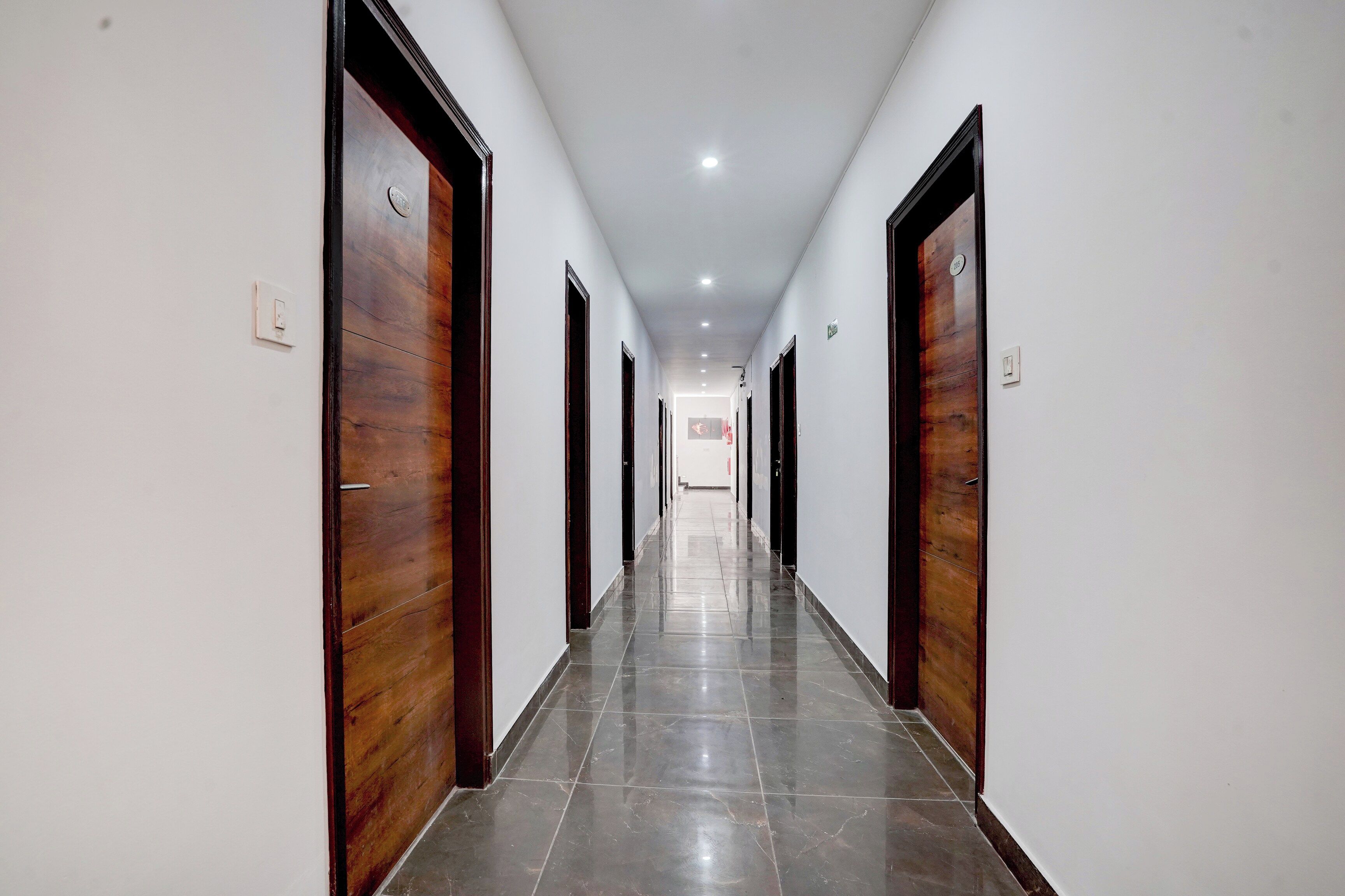 Un pasillo largo y estrecho con puertas de madera a ambos lados y suelo de baldosas.