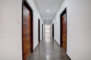 Un pasillo largo y estrecho con puertas de madera a ambos lados y suelo de baldosas.