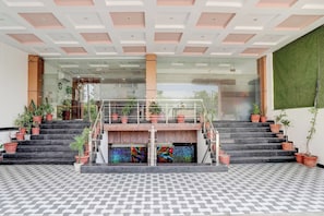 Una entrada de edificio moderna con fachada de vidrio, una escalera con plantas en macetas y un suelo con diseño.