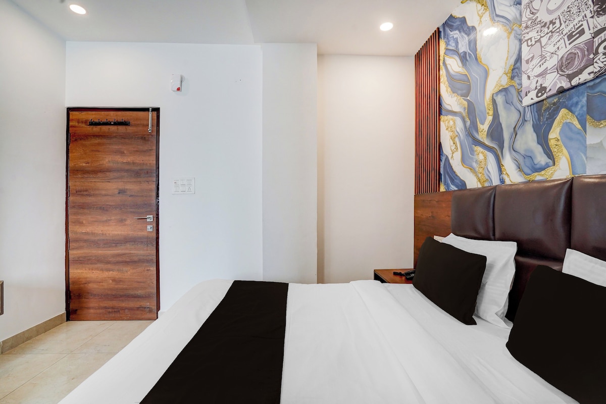 A hotel room with a wooden door, a bed with black and white bedding, and a wall with a colorful abstract mural.