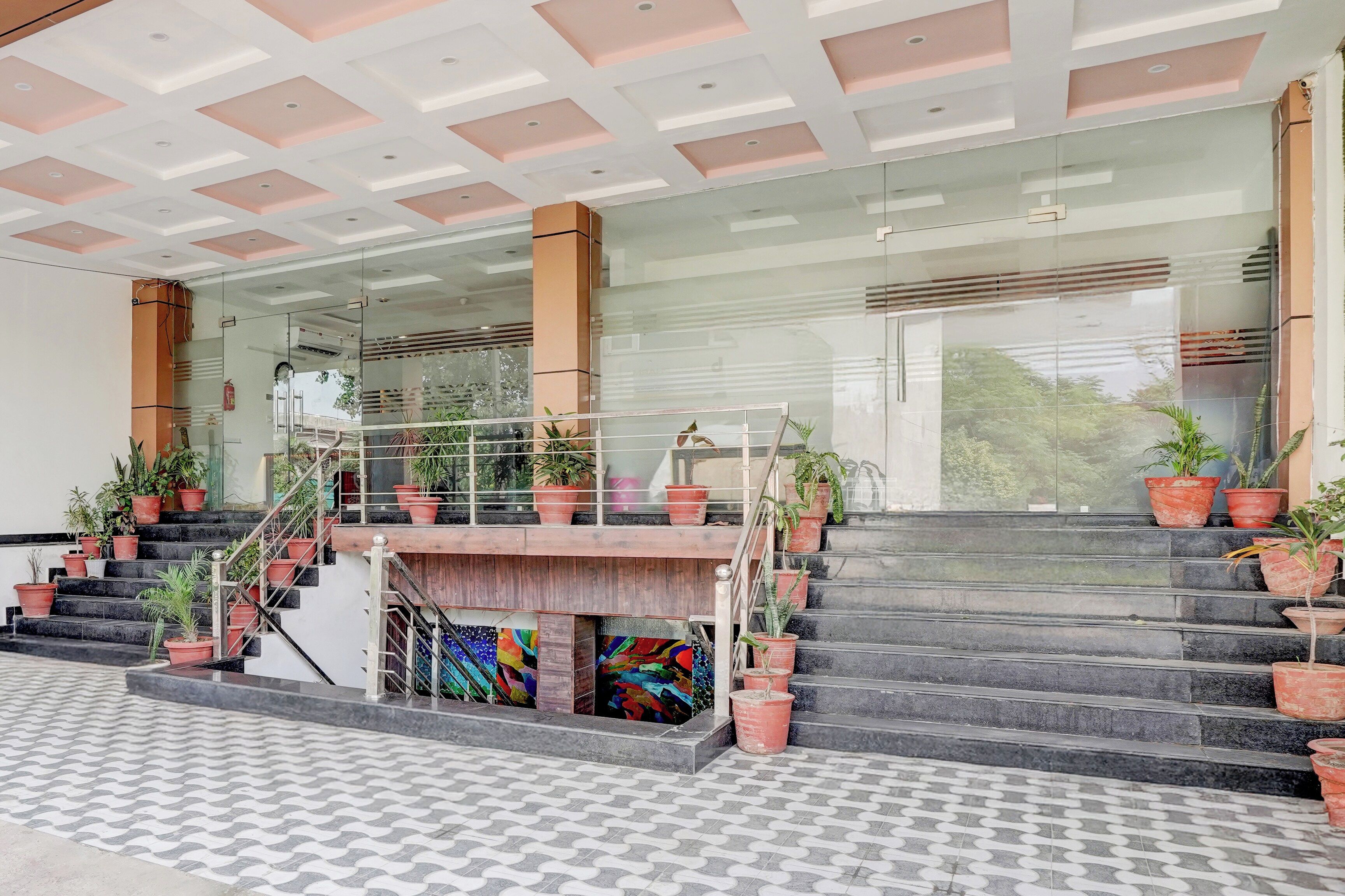 A building entrance with a staircase, potted plants, and a glass facade.