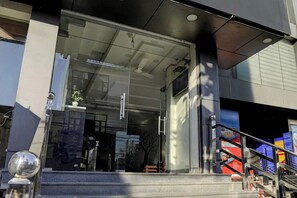A modern building entrance with a glass door, a small potted plant, and a staircase leading to the entrance. - Super Collection O Prem Nagar Dehradun (Dehradun)