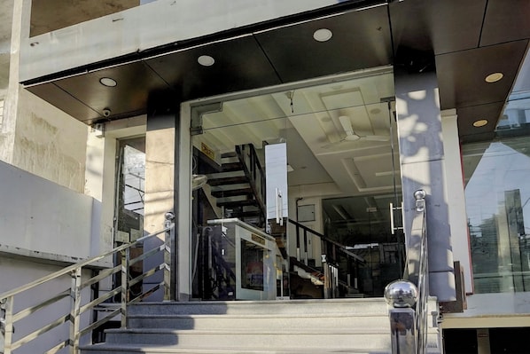 A modern building entrance with a glass door, metal stairs, and a metal railing.