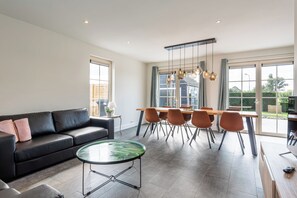 A modern living room with a sofa, a round coffee table, and a dining area with chairs and a table. - New Listing (Cadzand)