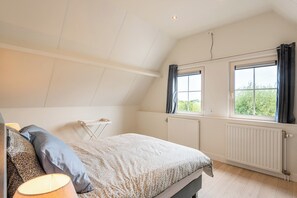 A bedroom with a bed, a nightstand, a lamp, and a window with curtains. - New Listing (Cadzand)