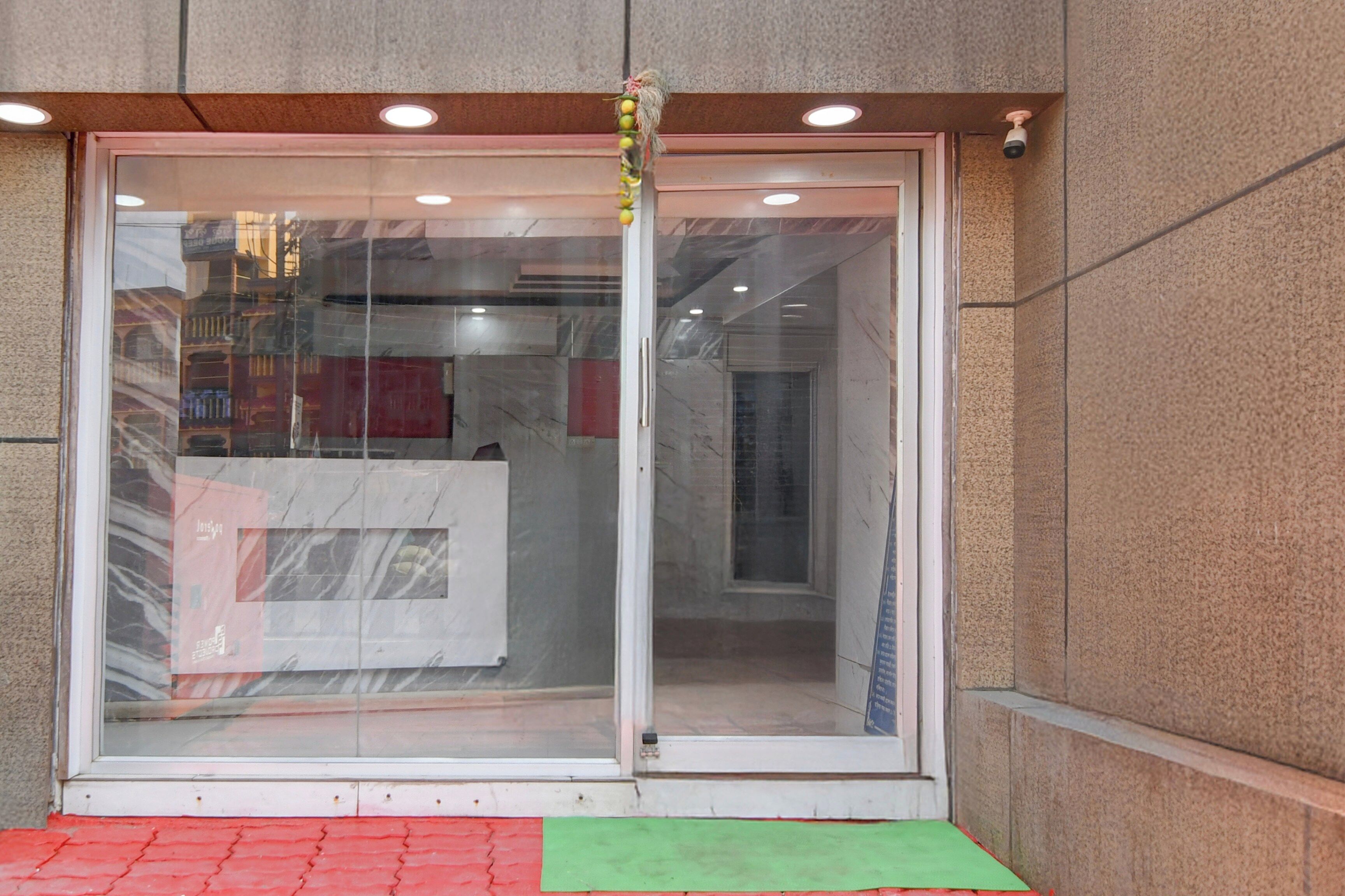 Une entrée d’immeuble avec une porte en verre, une caméra de surveillance et un paillasson rouge et vert à la base.