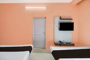 A hotel room with two beds, a television mounted on the wall, a bedside table with a phone and a power outlet, and a door with a handle.
