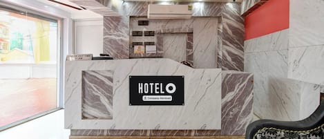 A hotel reception desk with a marble finish, a sign indicating check-out time, and a company-serviced label.