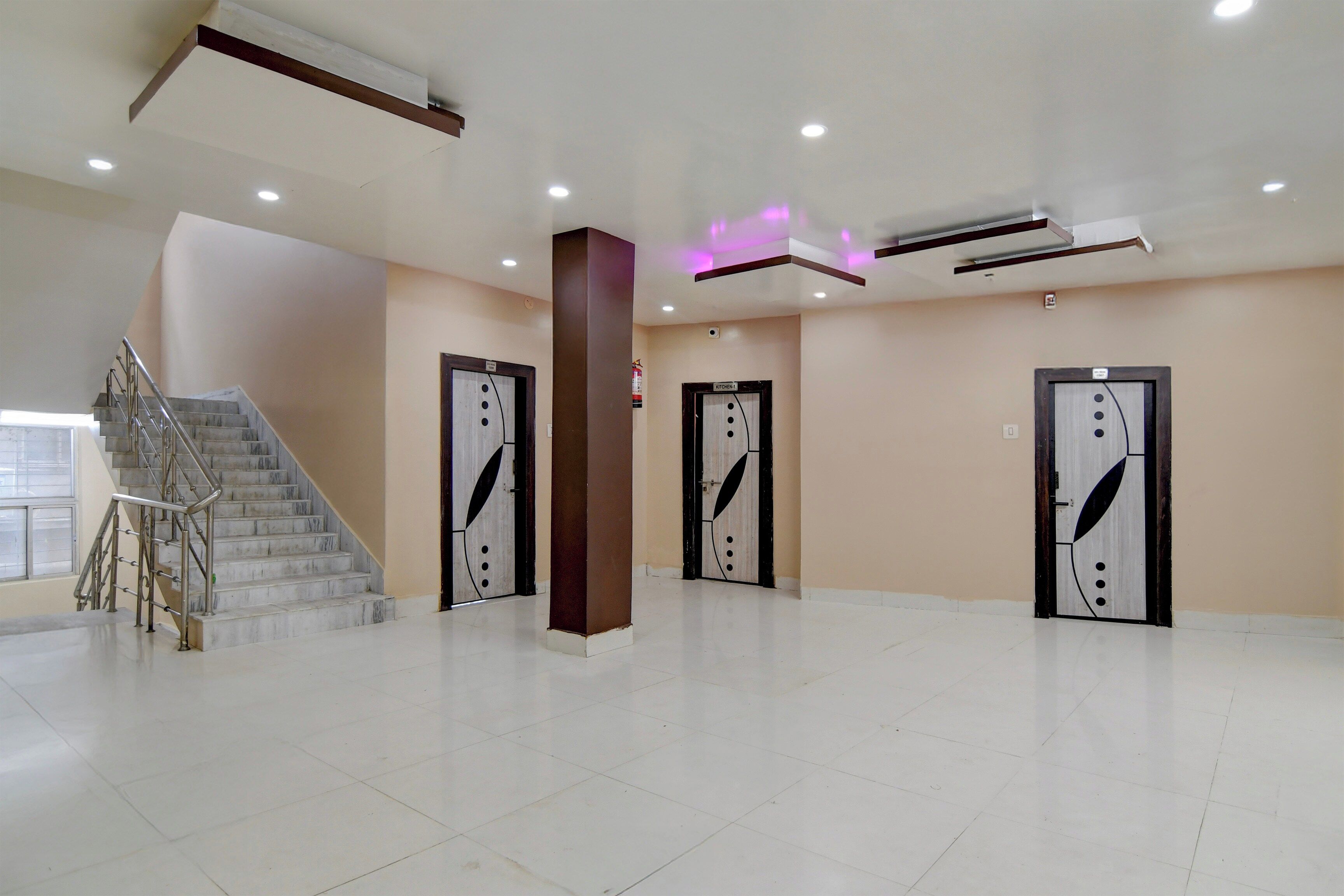 A spacious lobby with a marble staircase, three doors with decorative handles, and a modern ceiling with recessed lighting.
