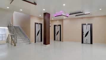 A spacious lobby with a marble staircase, three doors with decorative handles, and a modern ceiling with recessed lighting.