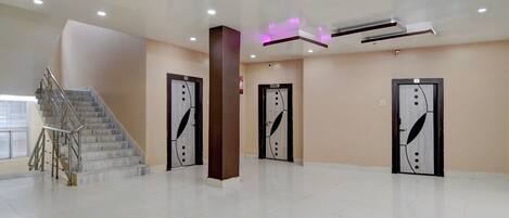 A spacious lobby with a marble staircase, three doors with decorative handles, and a modern ceiling with recessed lighting.