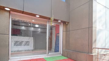 A building entrance with a glass door, a security camera, and a red and green mat outside.