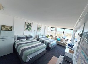 Habitación de hotel con dos camas, un escritorio, una silla, un refrigerador y ventanas amplias.