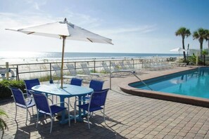 Zona junto a la piscina con mesa y sillas, una piscina y vistas a la playa.
