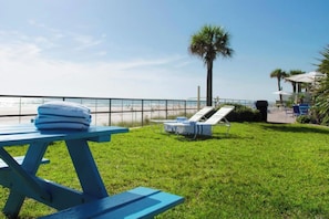 Un espacio al aire libre con césped, una mesa, sillones de descanso, una palmera y vistas a la playa.