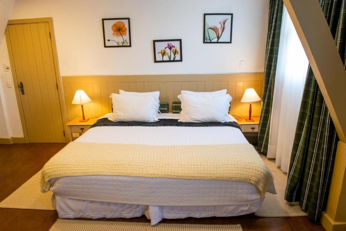 A hotel room with a bed, two bedside lamps, a door, and three framed floral artworks on the wall.