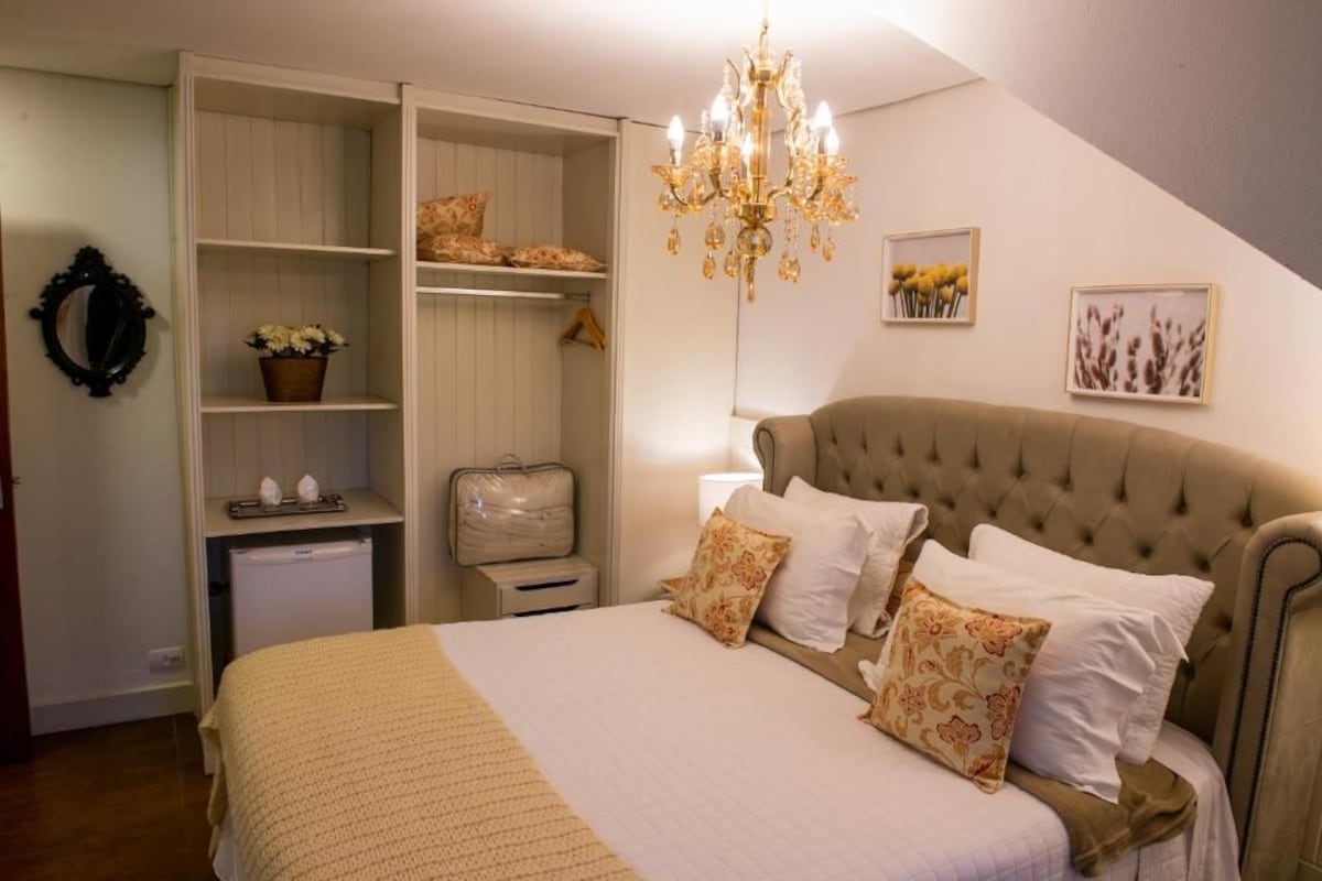 A bedroom with a bed, a chest of drawers, a wardrobe, a chandelier, and wall art.