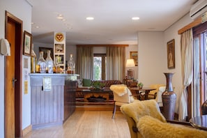 A well-lit living room with a sofa, armchairs, a coffee table, and a dining table. There is a bar area with bottles and a sign. - POUSADA DAS LAVANDAS (Campos do Jordão)
