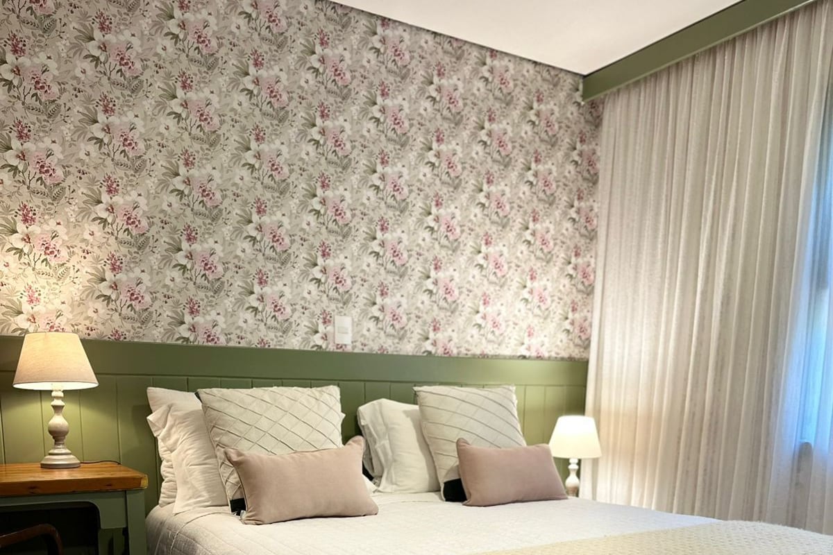 A bedroom with a large bed, a headboard, a nightstand, a lamp, a chair, and a window with curtains.