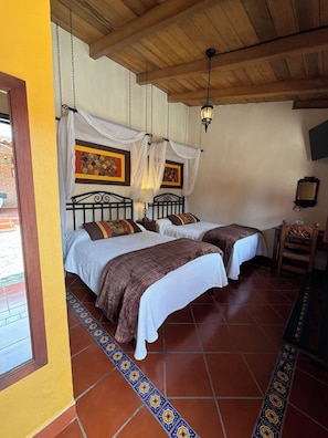 A room with two beds, a wooden ceiling, and a patterned floor.