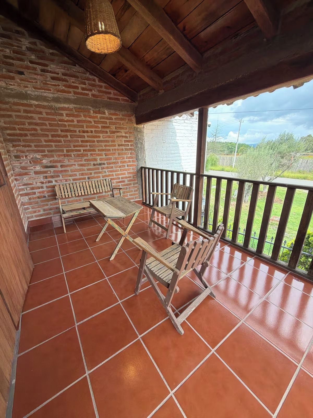 Un patio cubierto con pared de ladrillo, mobiliario de madera y vistas al campo.