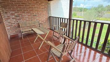 Un patio cubierto con pared de ladrillo, mobiliario de madera y vistas al campo.