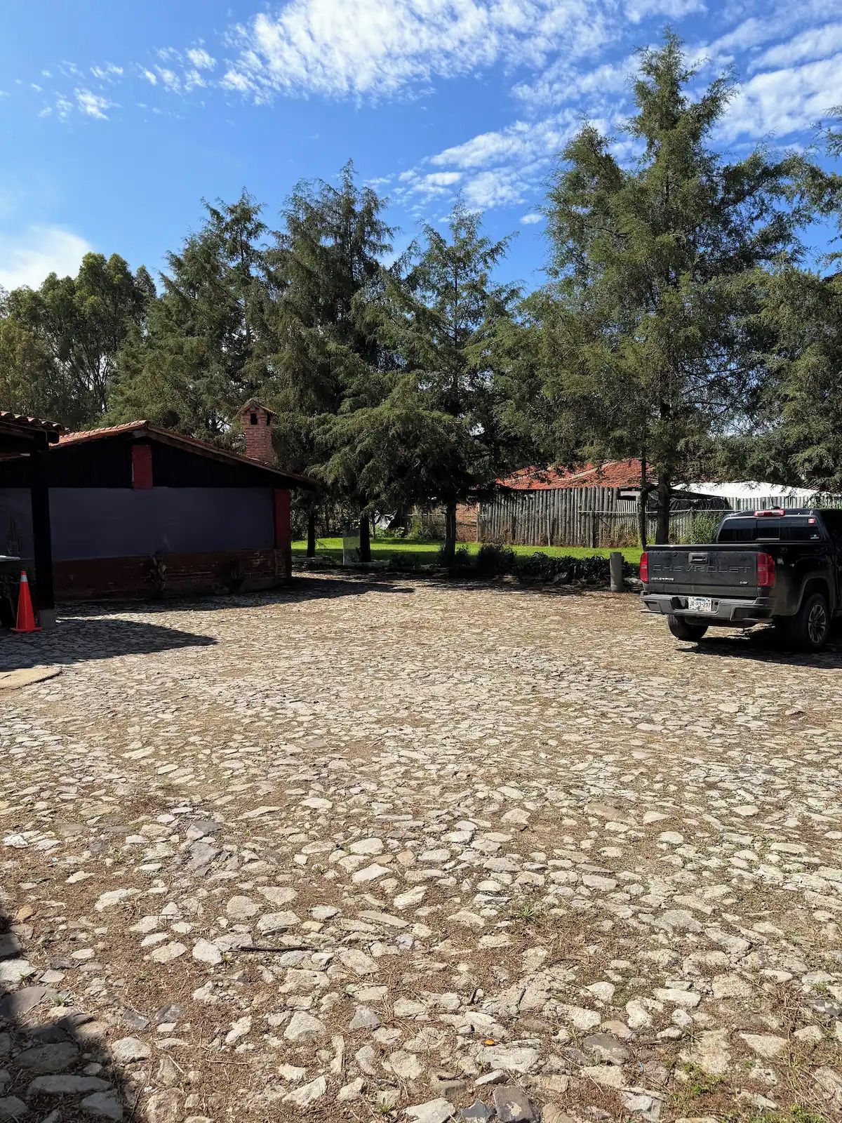 Uma entrada de cascalho leva a um edifício com telhado vermelho, cercado por árvores e um caminhão estacionado.