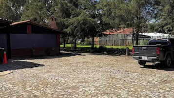 Uma entrada de cascalho leva a um edifício com telhado vermelho, cercado por árvores e um caminhão estacionado.