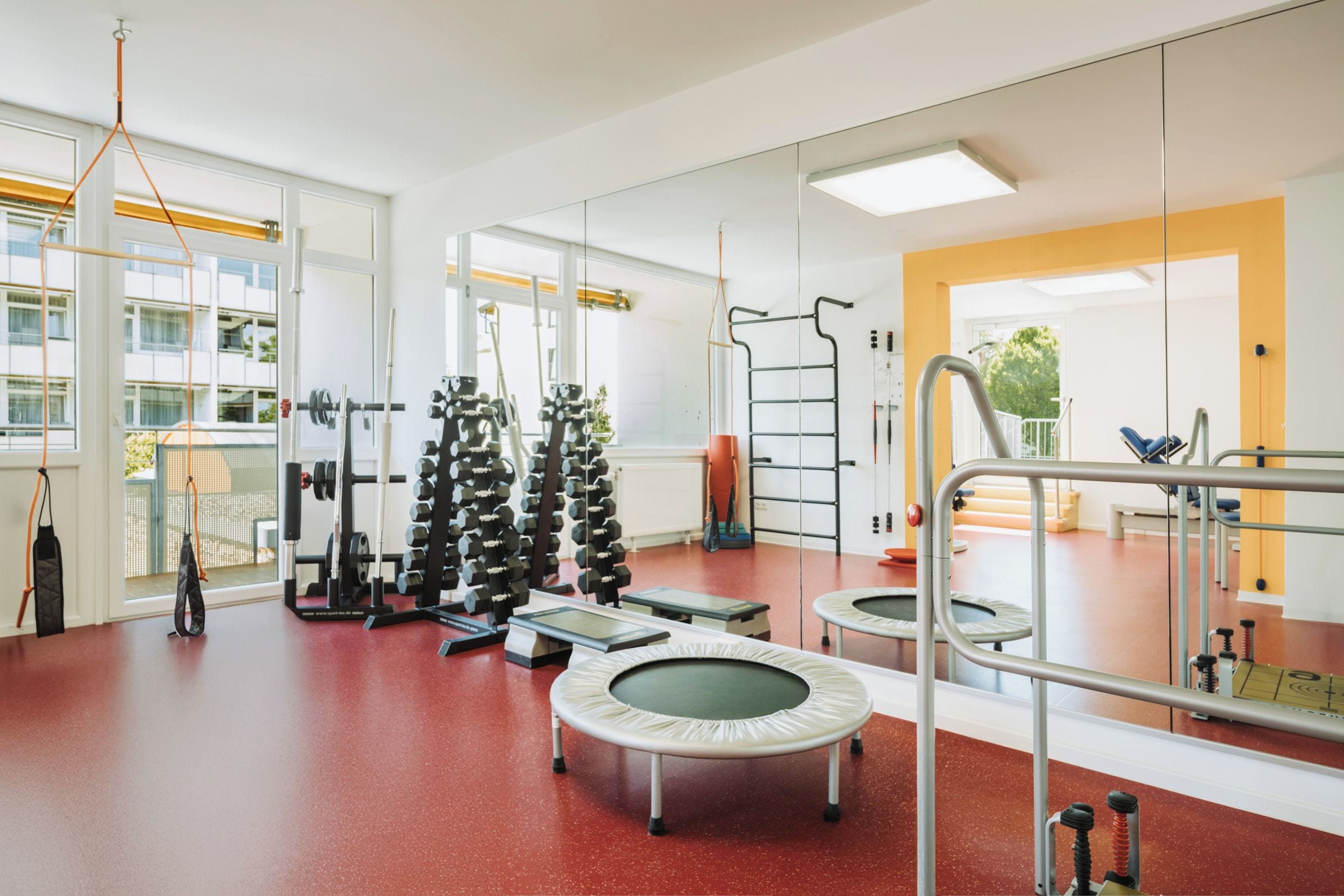 Ein Fitnessraum mit Trainingsgeräten, einer Hüpfmatte und einem großen Spiegel.