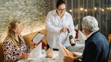 Een restaurantscène, een ober schenkt wijn in voor een gast.