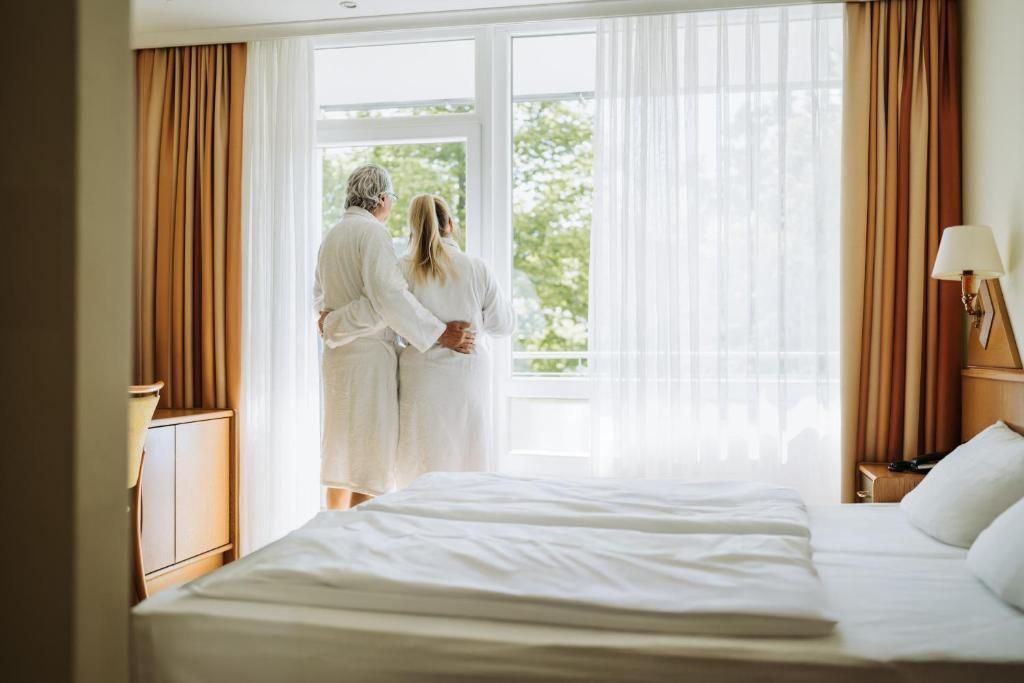 Ein Hotelzimmer mit einem großen Bett, einem Nachttisch, einer Lampe und einem Fenster mit Vorhängen.