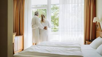 Ein Hotelzimmer mit einem großen Bett, einem Nachttisch, einer Lampe und einem Fenster mit Vorhängen.