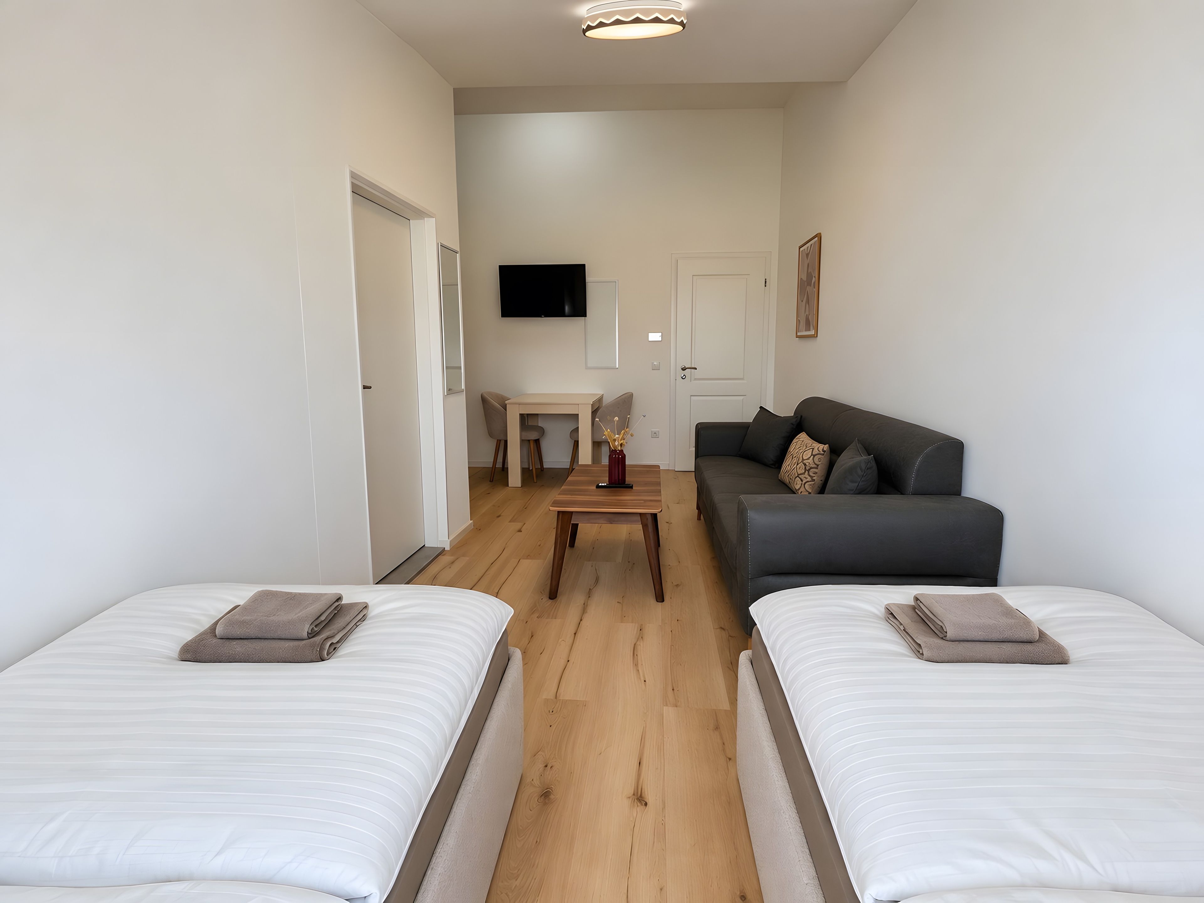 Une chambre d’hôtel moderne avec deux lits, un canapé, une petite table et un téléviseur.