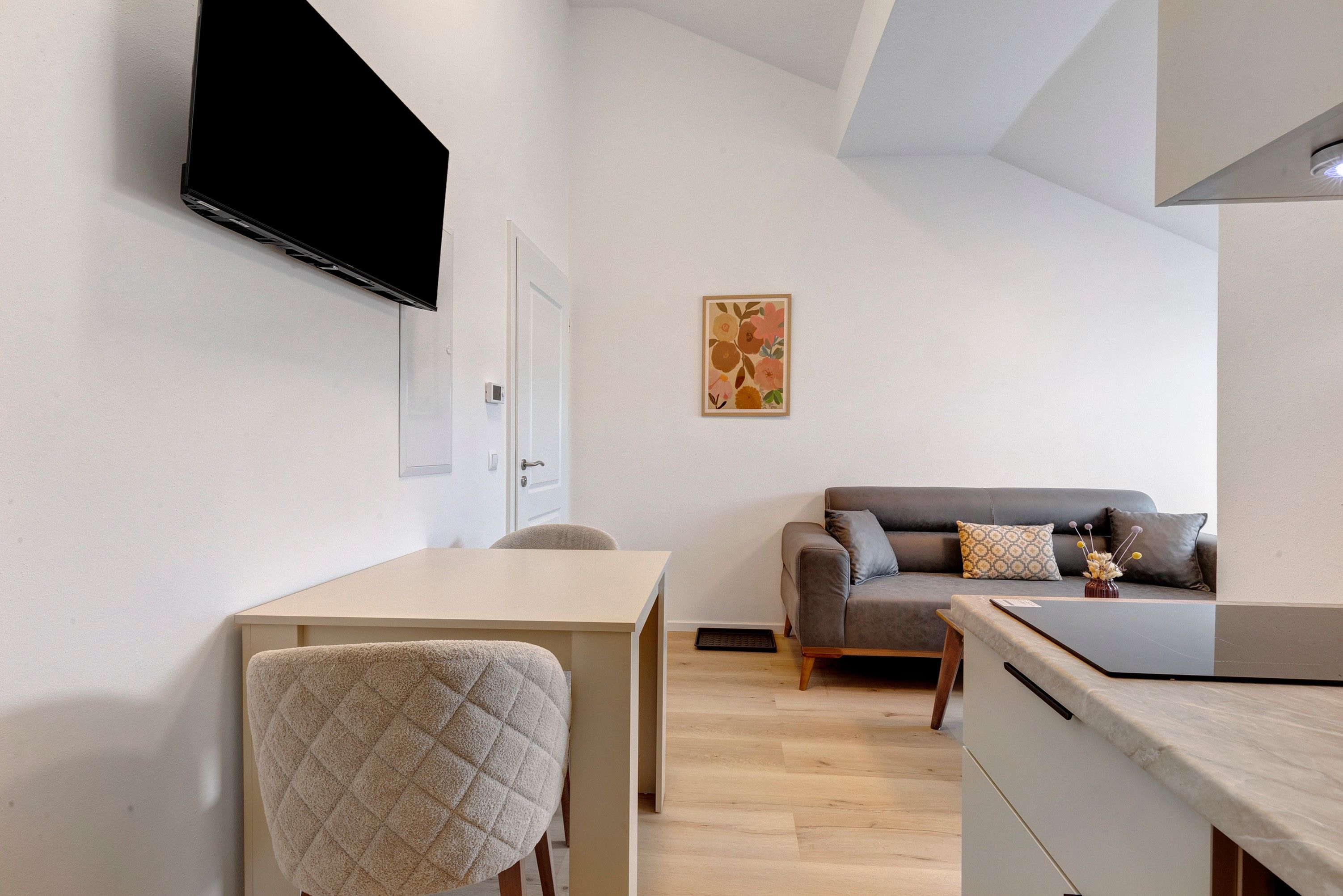 Un salon moderne avec un téléviseur à écran plat fixé au mur, un canapé agrémenté de coussins décoratifs, une petite table et un fauteuil.
