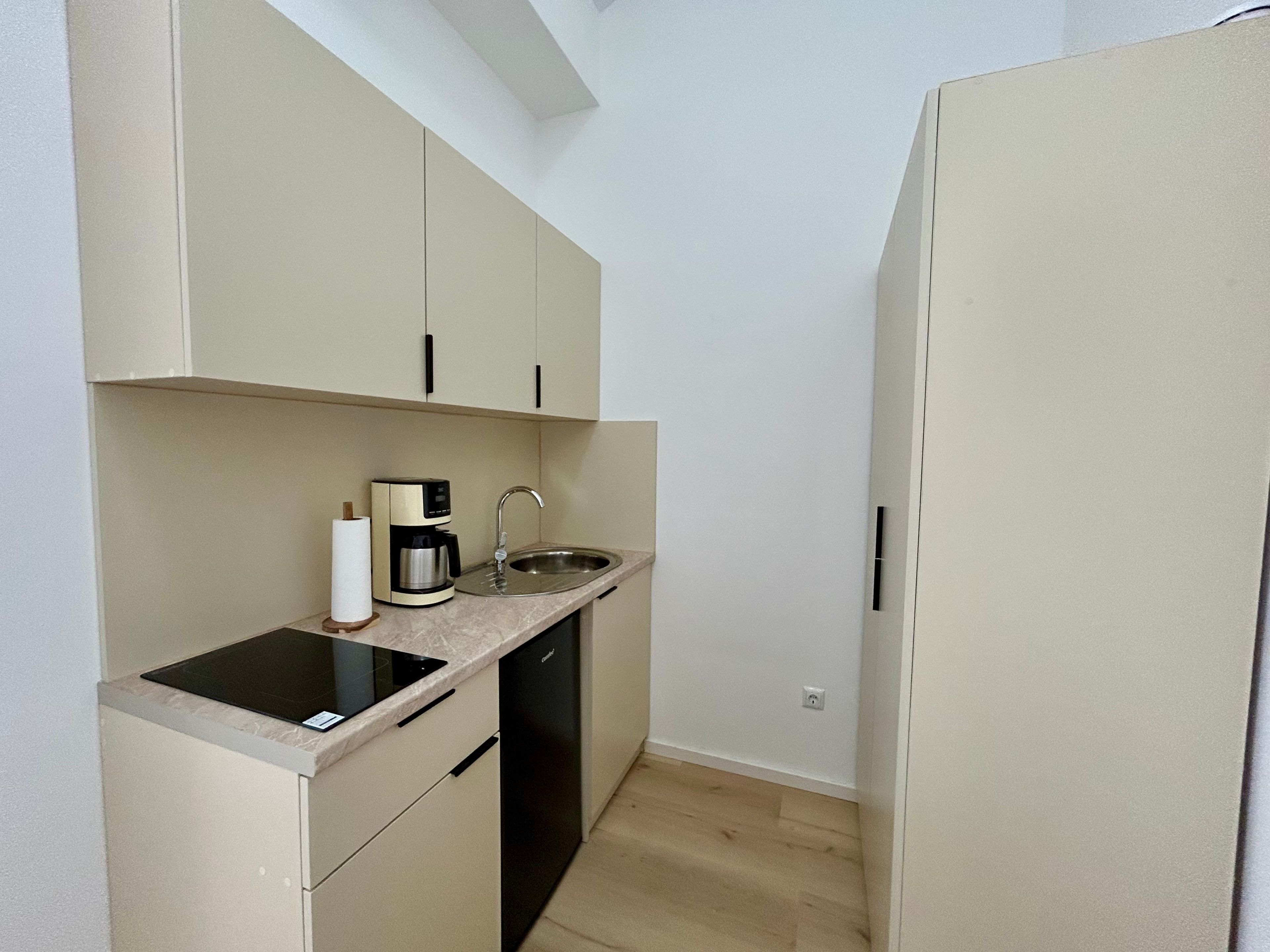 Una cucina compatta con piano cottura integrato, macchina del caffè, lavello e lavastoviglie.