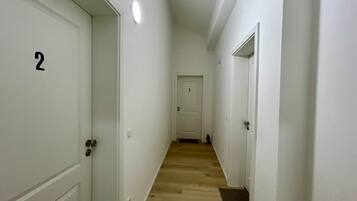 A narrow hallway with white doors numbered 2 and 3, wooden flooring, and a light fixture on the ceiling.