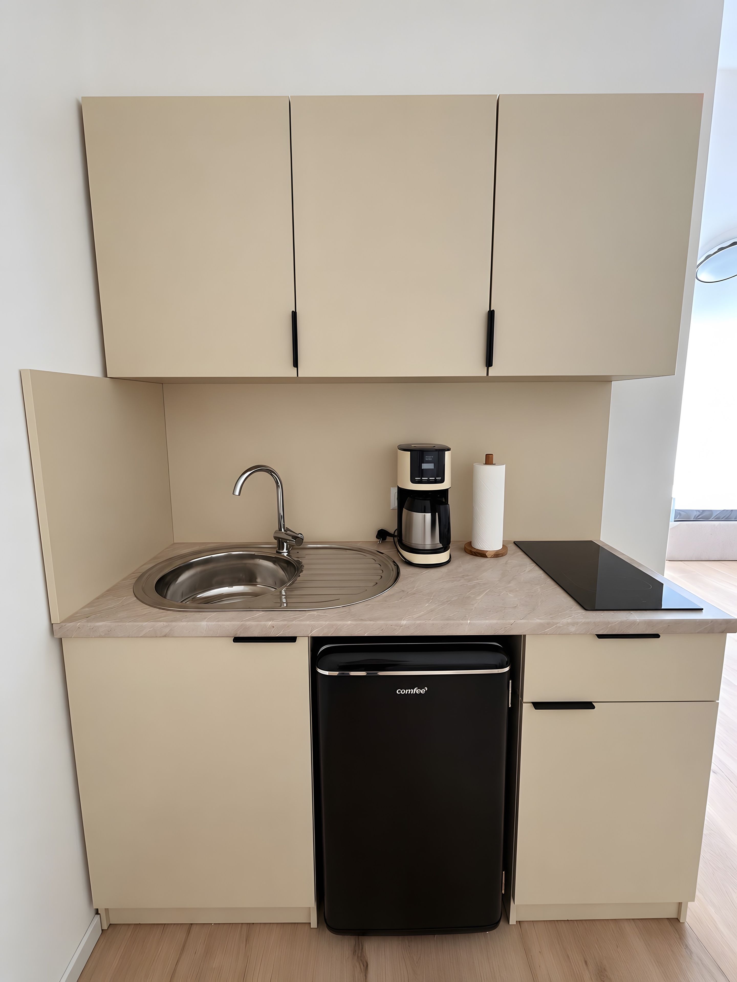 Una kitchenette compacta con un lavamanos, cafetera y un lavavajillas negro.