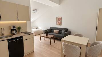 A modern kitchen with a dishwasher, a dining area with a table and chairs, a gray sofa, and a painting on the wall.