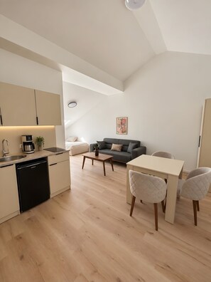 A modern kitchen with a dishwasher, a dining area with a table and chairs, a gray sofa, and a painting on the wall. - Apartment 'Nr. 3' with Wi-Fi (Jettingen-Scheppach)