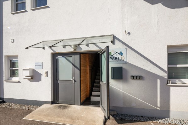 A building entrance with a glass door, a small porch, and a sign indicating 'PART 13'.