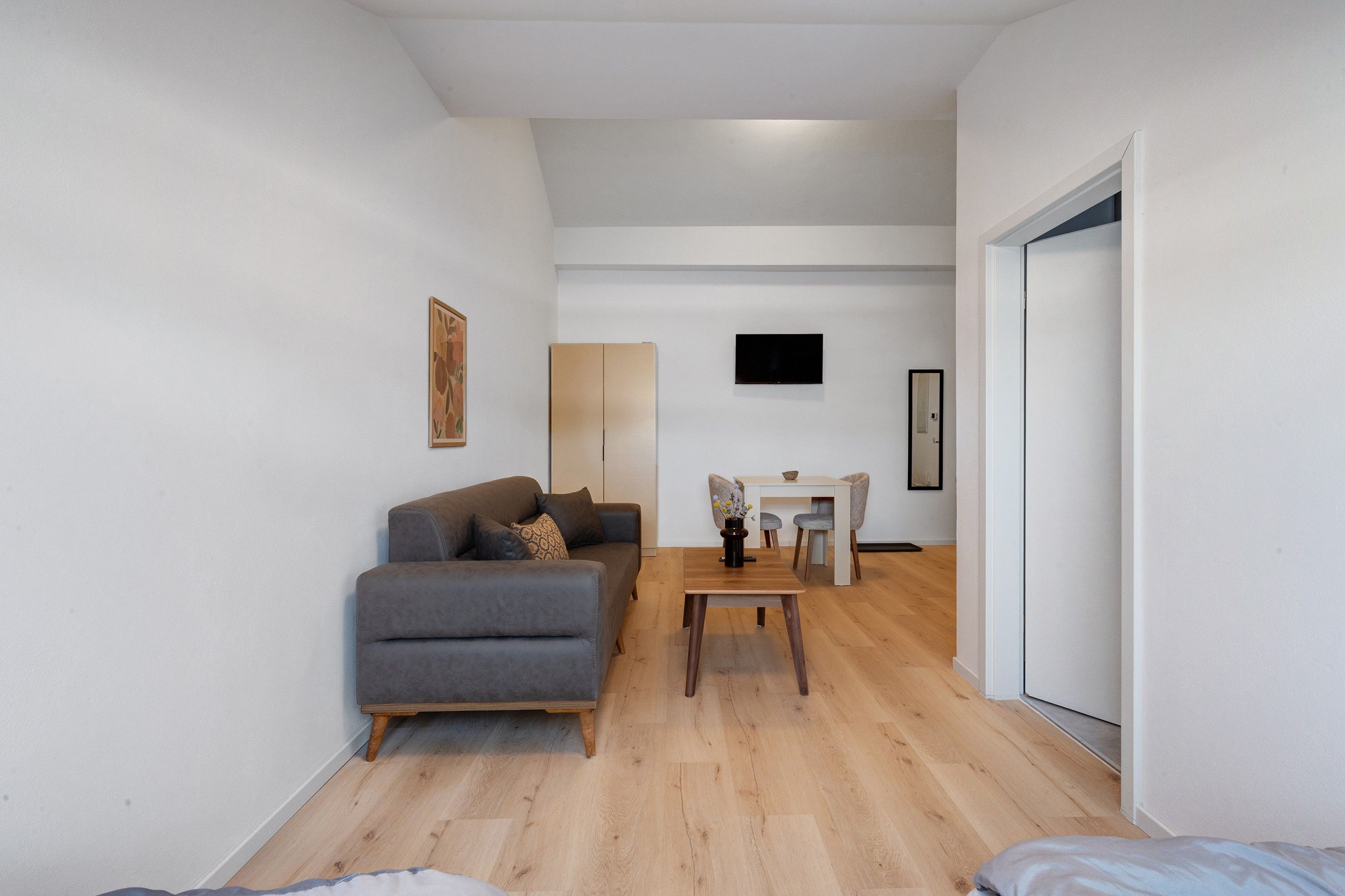 Ein modernes Wohnzimmer mit einem grauen Sofa, einem Holztisch und einem flachbildfernseher an der Wand.