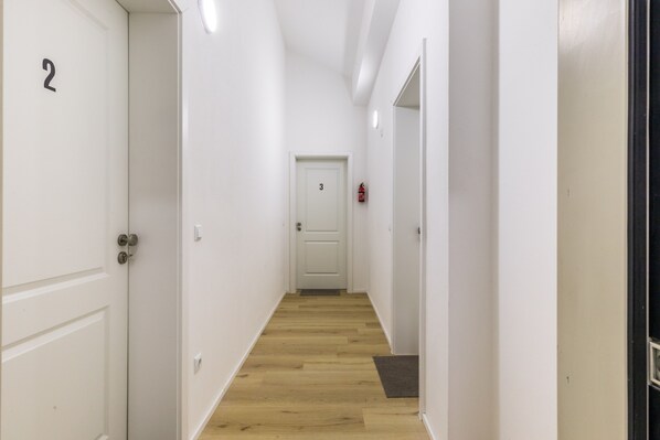 Un pasillo estrecho con suelo de madera, paredes blancas y puertas numeradas 2 y 3.