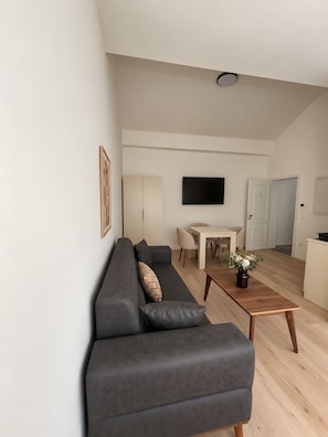 Un salon moderne avec un canapé gris, une table basse en bois et un téléviseur à écran plat fixé au mur.