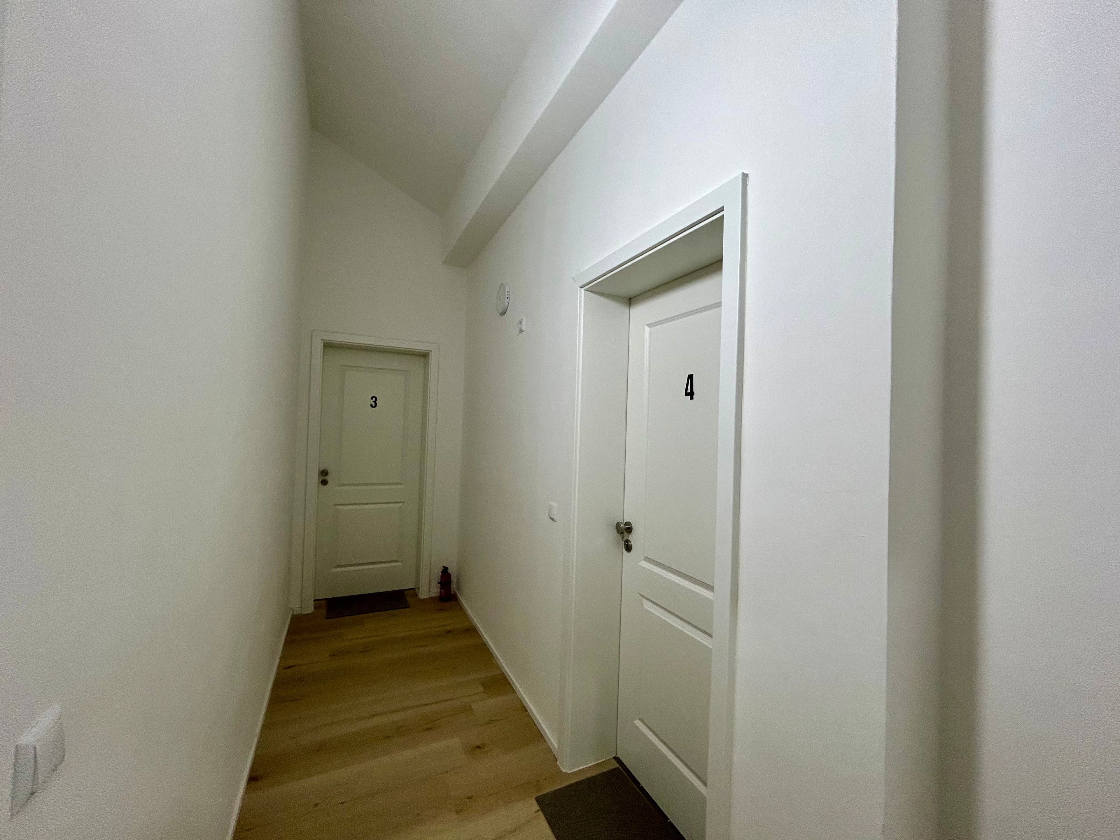 A narrow hallway with wooden flooring and white walls. There are two white doors, one with the number 3 and the other with the number 4.