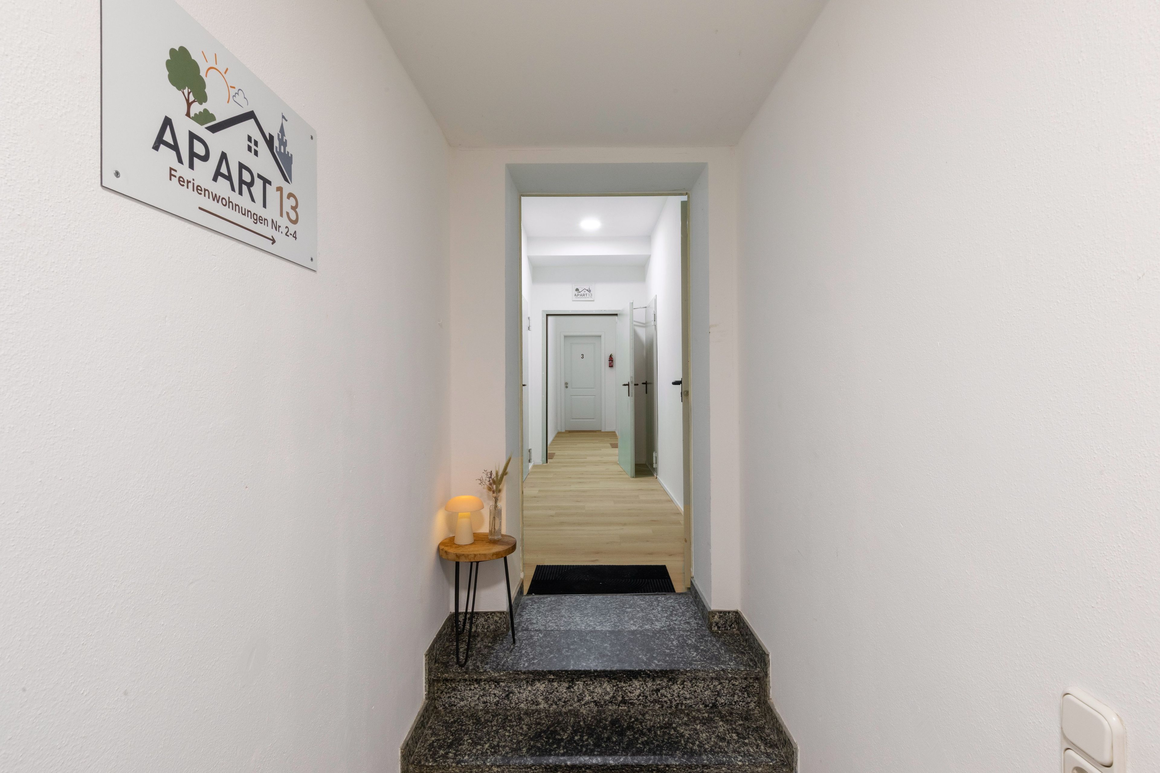 A hallway leading to a door labeled 'APART 13' with a sign indicating 'Wohnungen Nr. 2-4'.