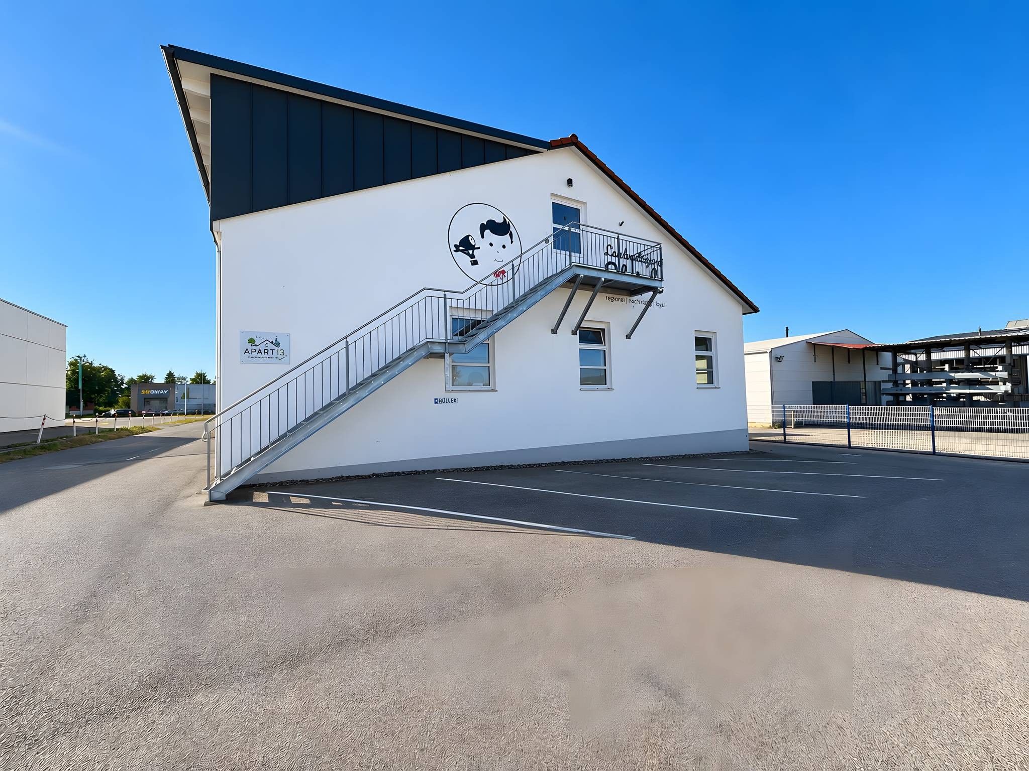 A building with a white facade, a black roof, and a staircase leading to a balcony.
