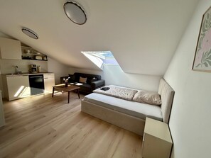 Ein kompakter Wohnbereich mit Küchenzeile, einer Couch, einem Esstisch und einem Oberlicht.