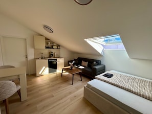 A compact living space with a kitchenette, a sofa, a dining table, and a window with a view. - Apartment 'Nr. 4' with Wi-Fi (Jettingen-Scheppach)